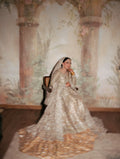 Bride wearing champagne silver embellished bridal gown with sweeping train and matching dupatta, seated in vintage mural backdrop - Èlaan Studio Pakistani wedding wear