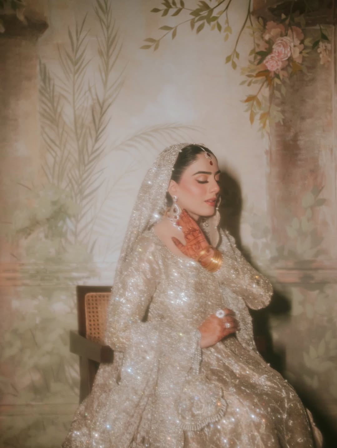 Bride wearing champagne silver embellished bridal gown with sweeping train and matching dupatta, seated in vintage mural backdrop - Èlaan Studio Pakistani wedding wear