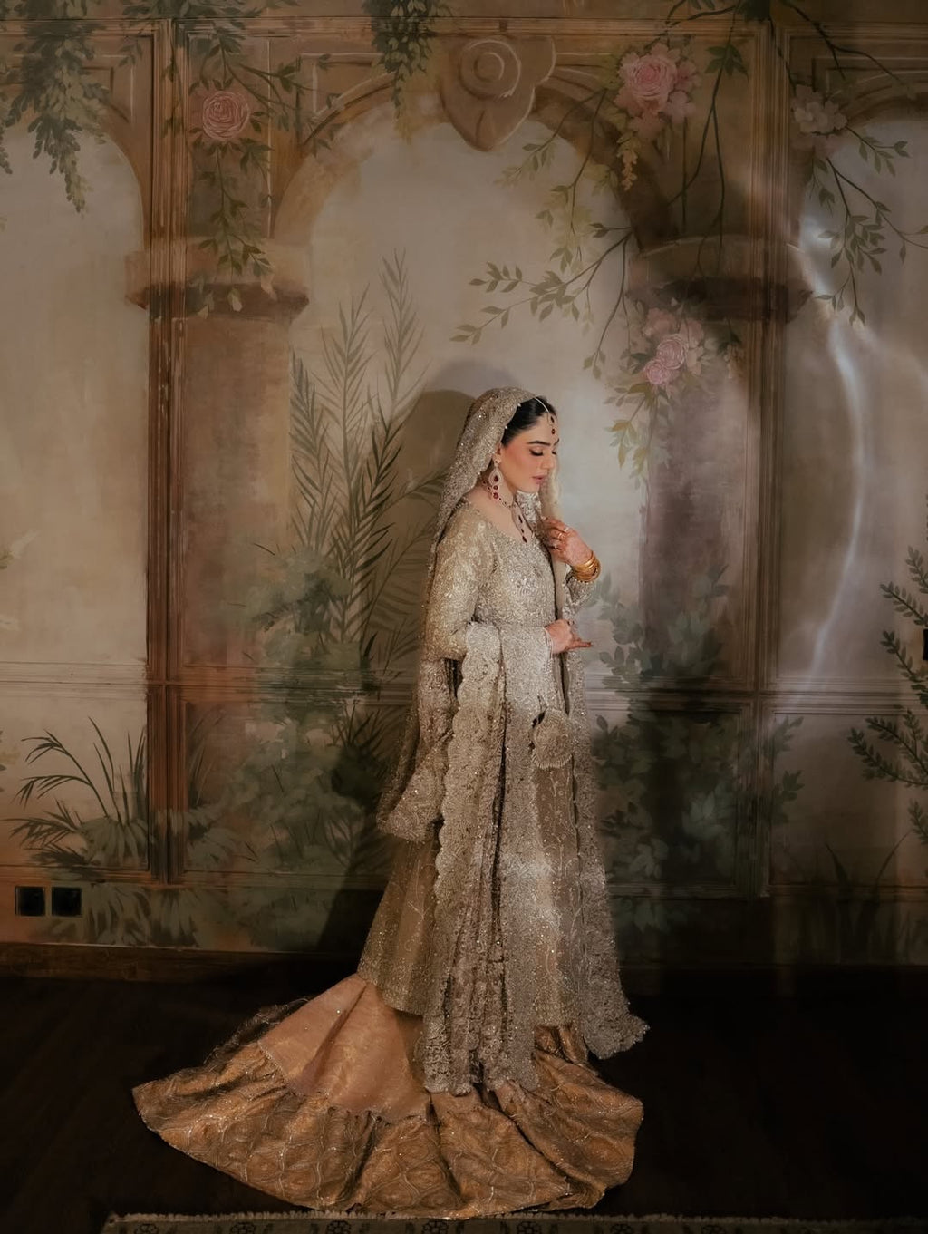 Bride wearing champagne silver embellished bridal gown with sweeping train and matching dupatta, seated in vintage mural backdrop - Èlaan Studio Pakistani wedding wear