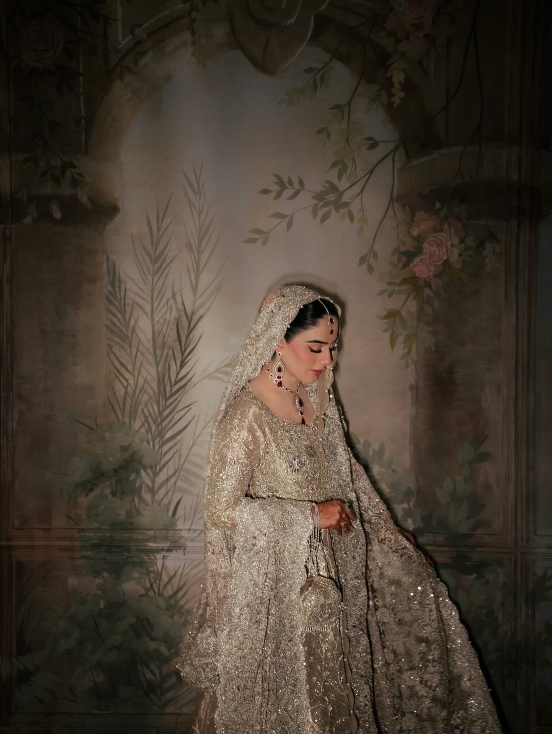 Bride wearing champagne silver embellished bridal gown with sweeping train and matching dupatta, seated in vintage mural backdrop - Èlaan Studio Pakistani wedding wear
