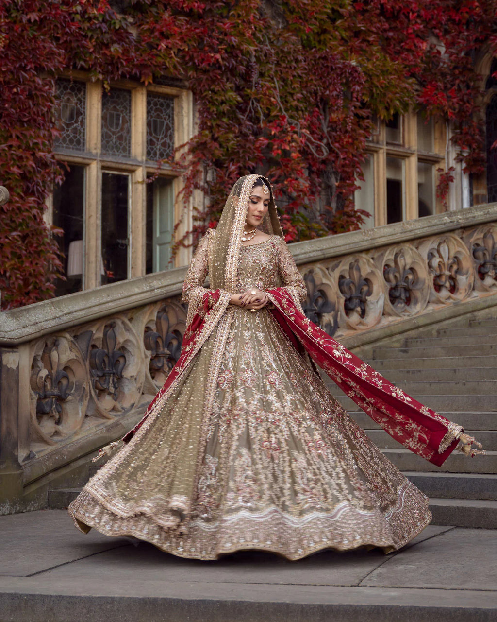 Bride wearing olive gold heavily embellished bridal lehenga with maroon embroidered dupatta, standing on stone staircase - Èlaan Studio Pakistani wedding wear