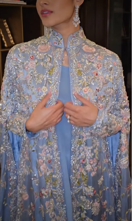Woman in dusty blue floral embroidered cape, side view showing floor-length drape
