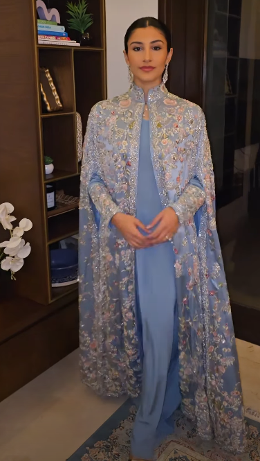Woman in dusty blue floral embroidered cape, side view showing floor-length drape