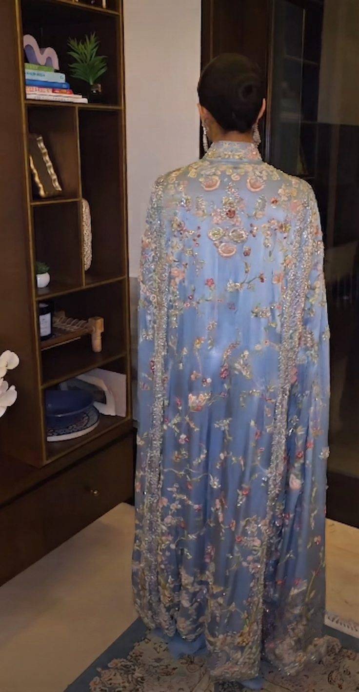 Woman in dusty blue floral embroidered cape, side view showing floor-length drape