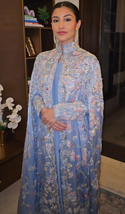 Woman in dusty blue floral embroidered cape, side view showing floor-length drape