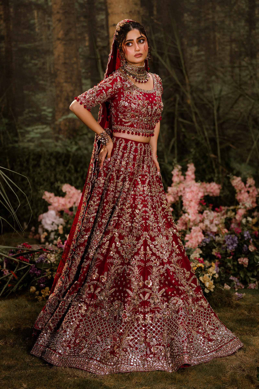 Bride wearing red bridal lehenga with dense gold zardozi embroidery, holding skirt outdoors in golden light - Èlaan Studio wedding wear