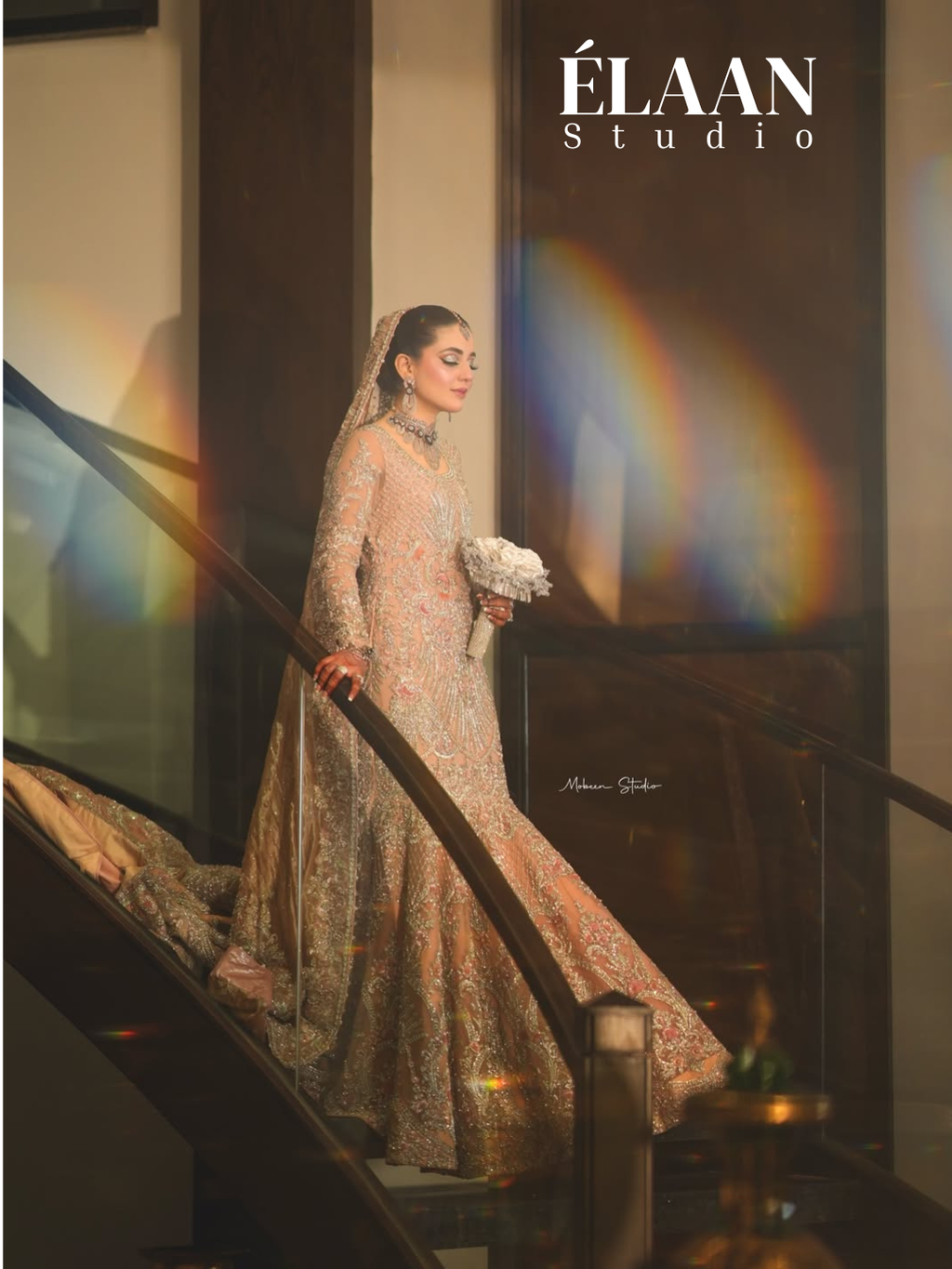 Bride wearing rose gold fully embellished fishtail bridal gown with dramatic train on staircase, holding bouquet - Èlaan Studio wedding wear