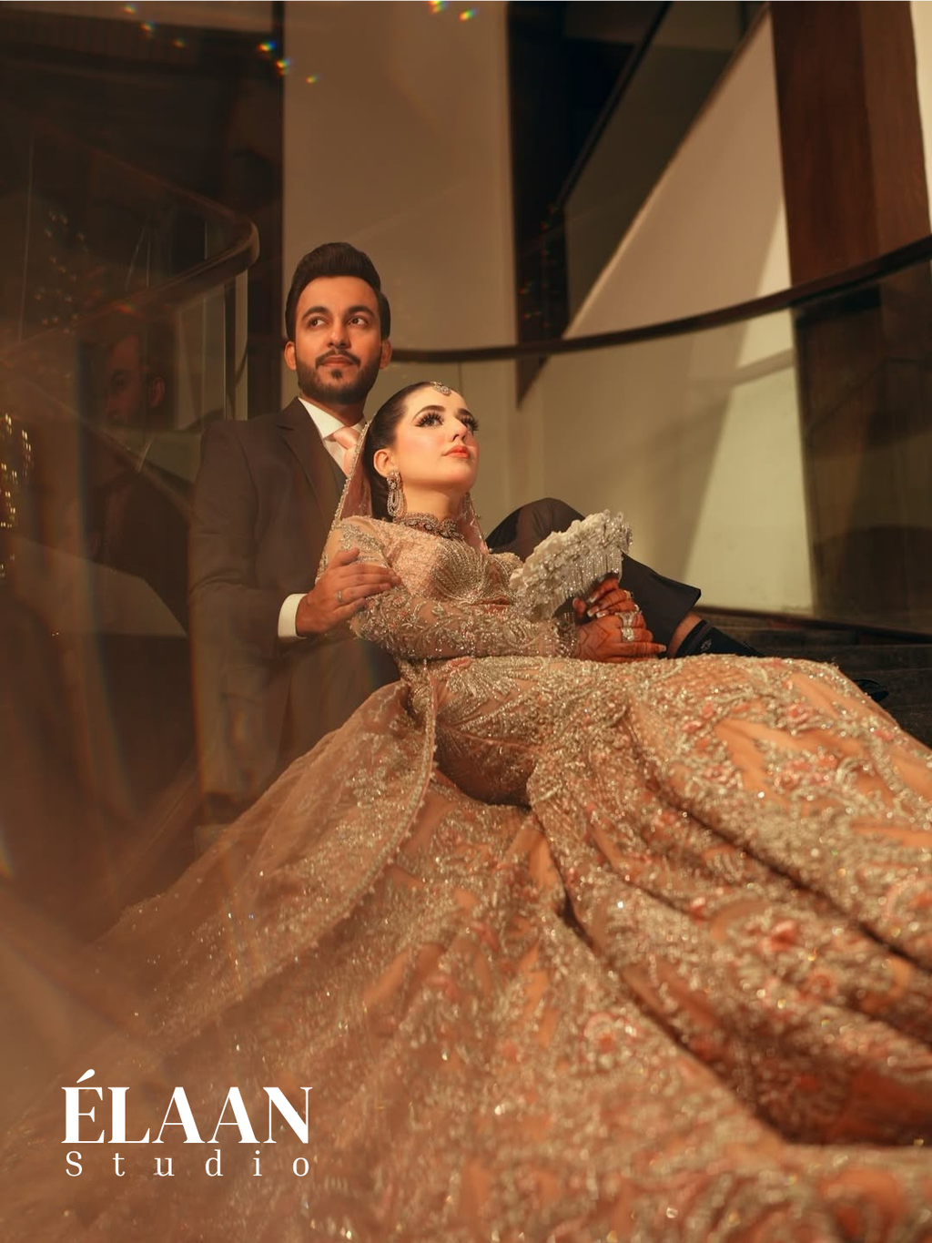Bride wearing rose gold fully embellished fishtail bridal gown with dramatic train on staircase, holding bouquet - Èlaan Studio wedding wear