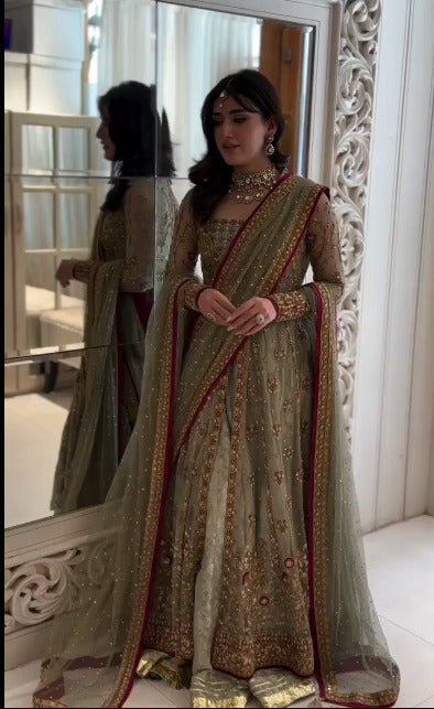 Bride wearing olive green embellished lehenga with maroon bordered dupatta, standing in front of ornate mirror - Èlaan Studio bridal wear