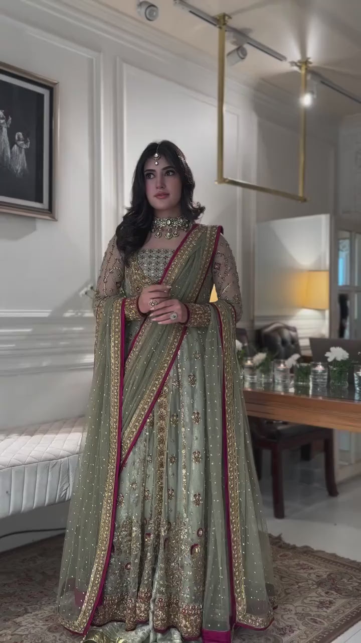 Bride wearing olive green embellished lehenga with maroon bordered dupatta, standing in front of ornate mirror - Èlaan Studio bridal wear